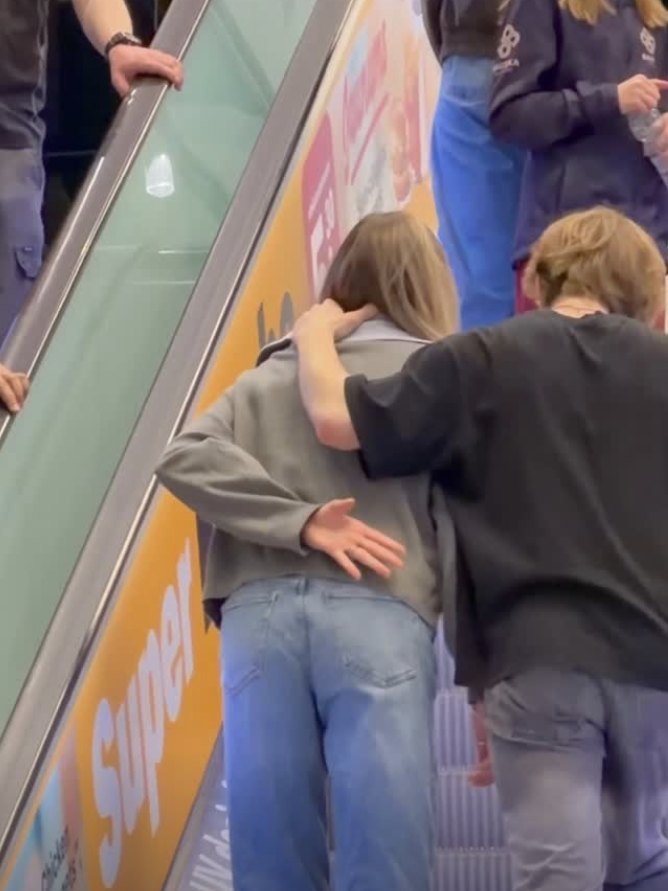 On an escalator, a hand behind a back makes the Signal for Help